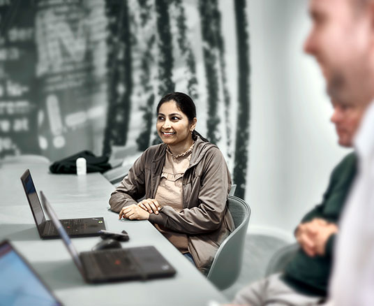 3 people at a meeting table with laptops open looking off camera left